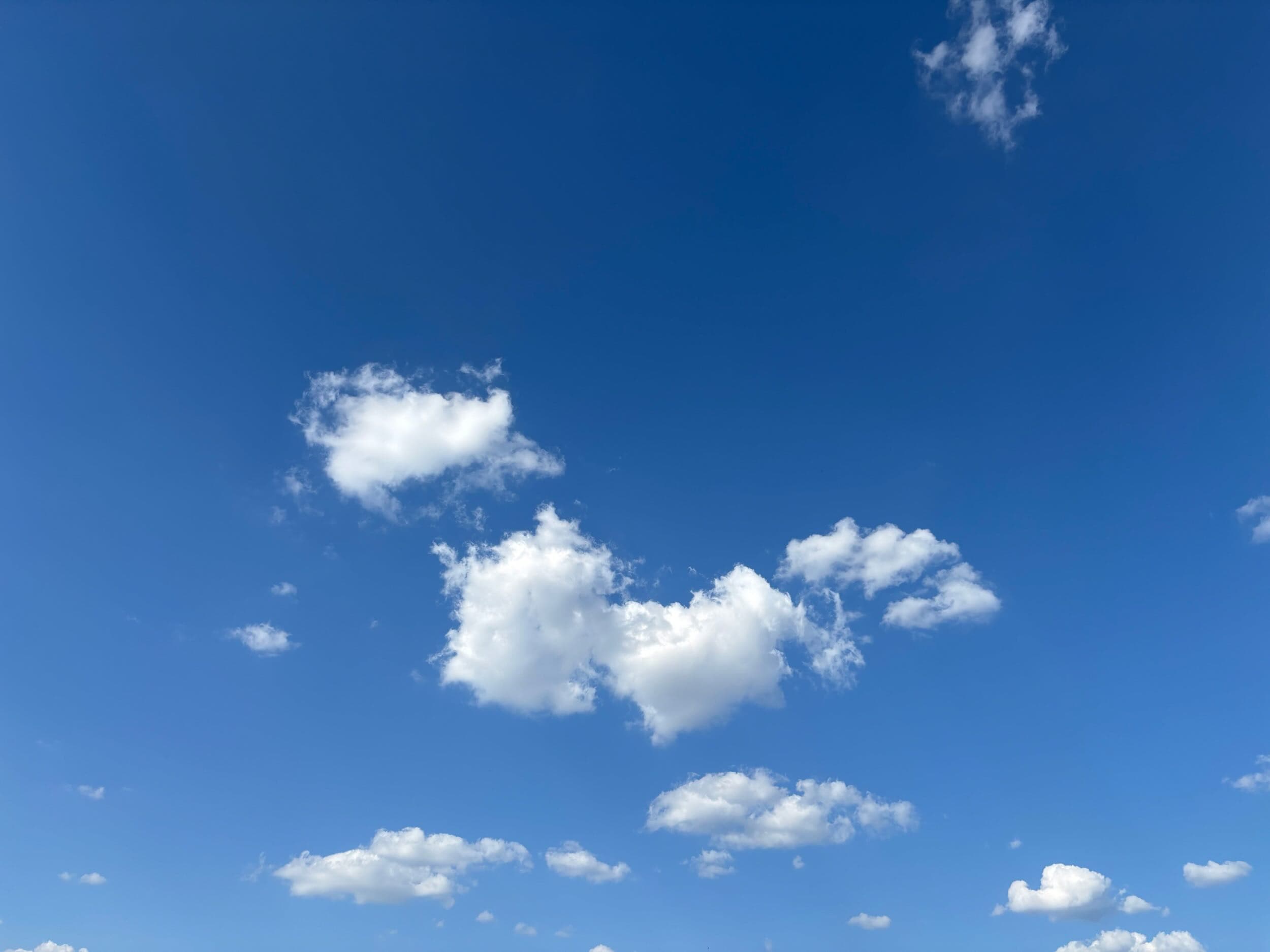 A bright blue sky with scattered fluffy white clouds, including a few larger cloud clusters near the center and smaller ones drifting across the open space.